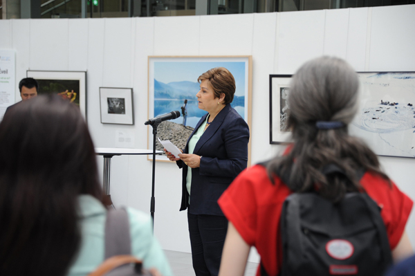 Une femme parle dans un microphone avec des œuvres d'art installées en arrière-plan. Vue du point de vue du public.