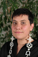 Un portrait d’une femme aux cheveux foncés et courts, portant des pendants d’oreille qui tombent plus bas que ses épaules.