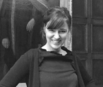 Une photo de tête d'une femme aux cheveux noirs ramenés en queue de cheval, portant un pull noir sur une chemise noire.