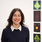 La photo d'une femme souriante aux longs cheveux noirs se trouve à côté de quatre petits tableaux installés verticalement sur un mur.